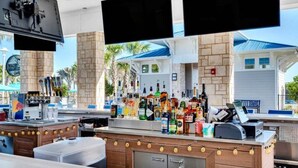 Un espace bar avec un comptoir, de nombreuses bouteilles d’alcool et un écran de télévision.