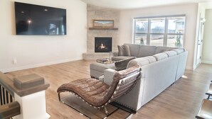 A modern living room with a stone fireplace, a large flat-screen TV, and a grey sectional sofa.