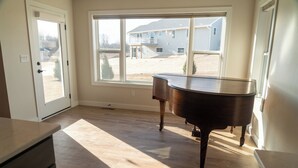 A room with a piano, a large window, and a door leading outside.