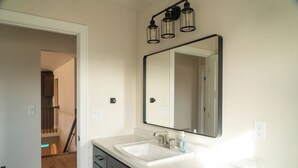 A bathroom with a white sink, a large mirror, and a light fixture above the mirror.