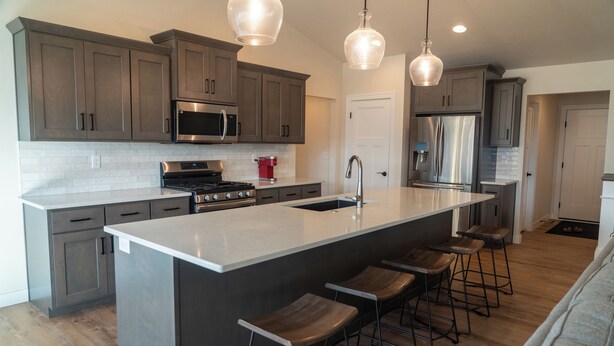 A modern kitchen with dark cabinets, stainless steel appliances, a large island with bar stools, and pendant lighting.