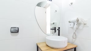 Ein modernes Badezimmer mit einem runden Spiegel, einem weißen Waschbecken, einem Fön und einem Handtuchhalter.