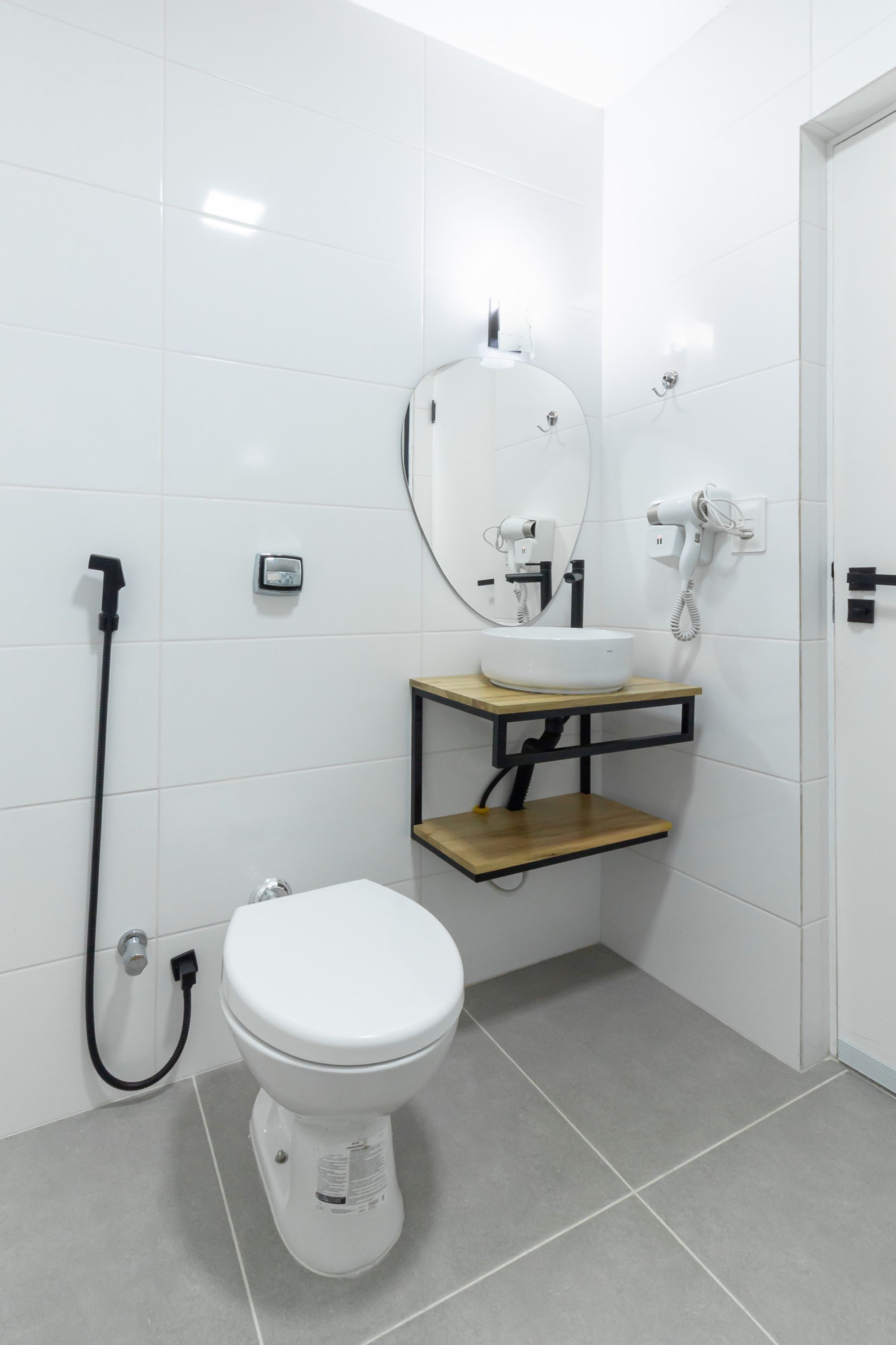 Un baño moderno con inodoro blanco, tocador de madera con espejo y ducha de mano.
