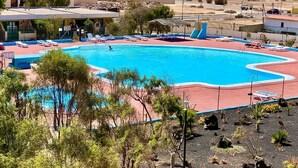 Una amplia piscina con tumbonas, rodeada de vegetación y edificios.