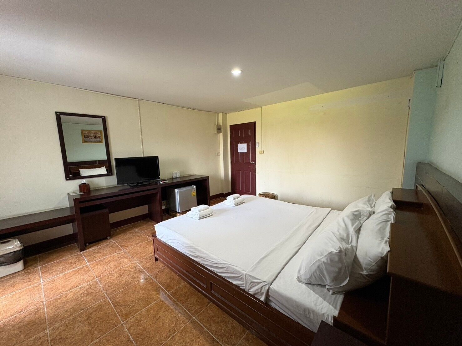 A hotel room with a bed, a desk with a television, a small refrigerator, and a door with a sign.