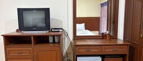 A hotel room with a wooden desk, a television, a mini-fridge, and a large mirror reflecting the room.