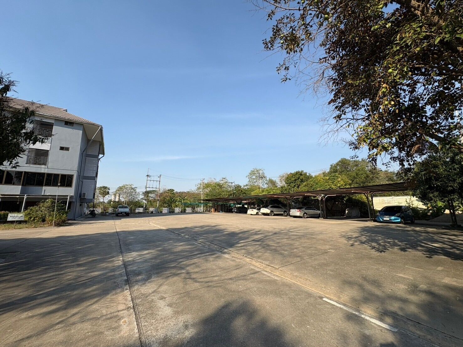 Un estacionamiento con varios autos, un edificio de techo inclinado y árboles al fondo.