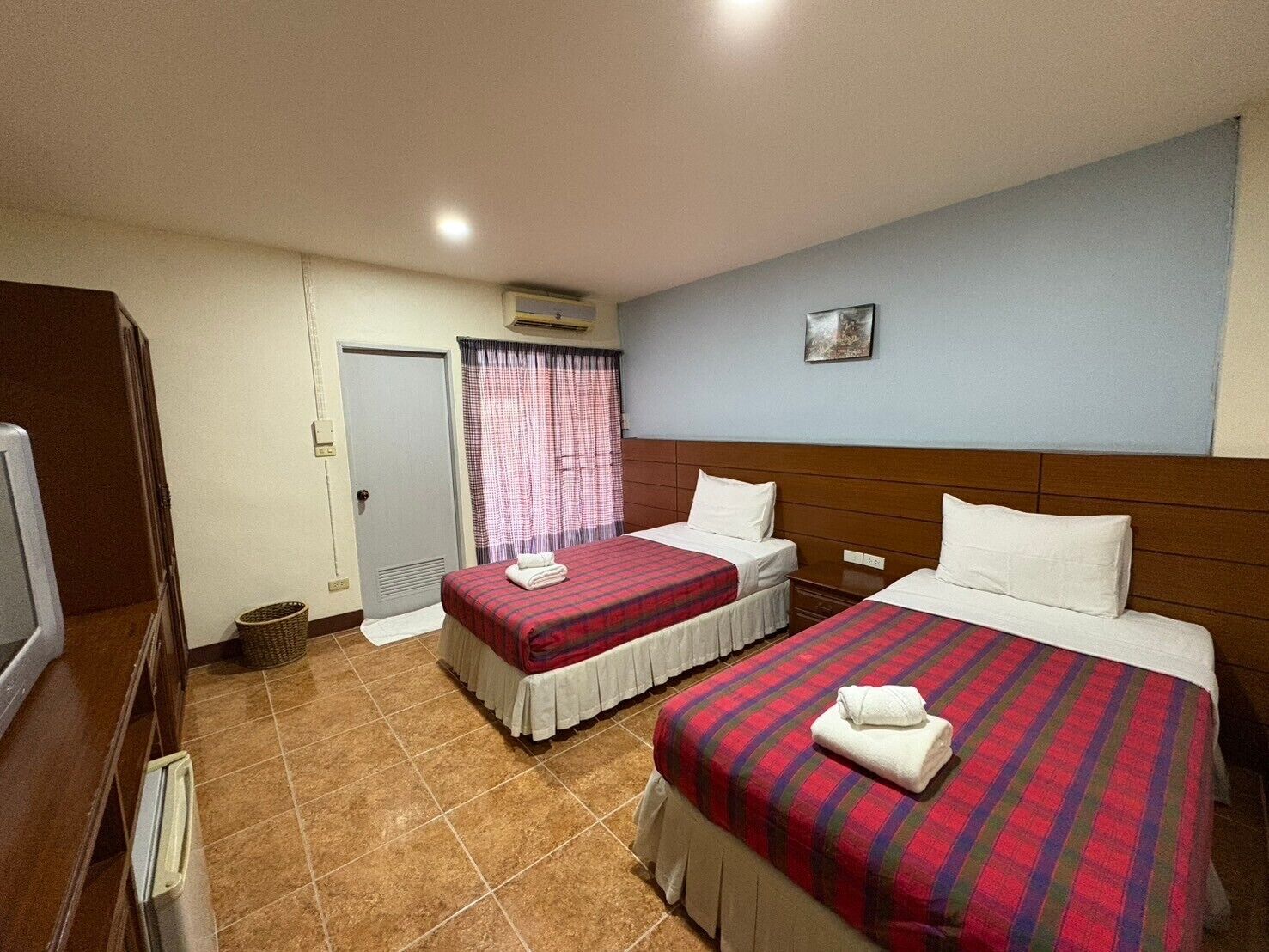 A hotel room with two beds, a television, a door, and a window with curtains.