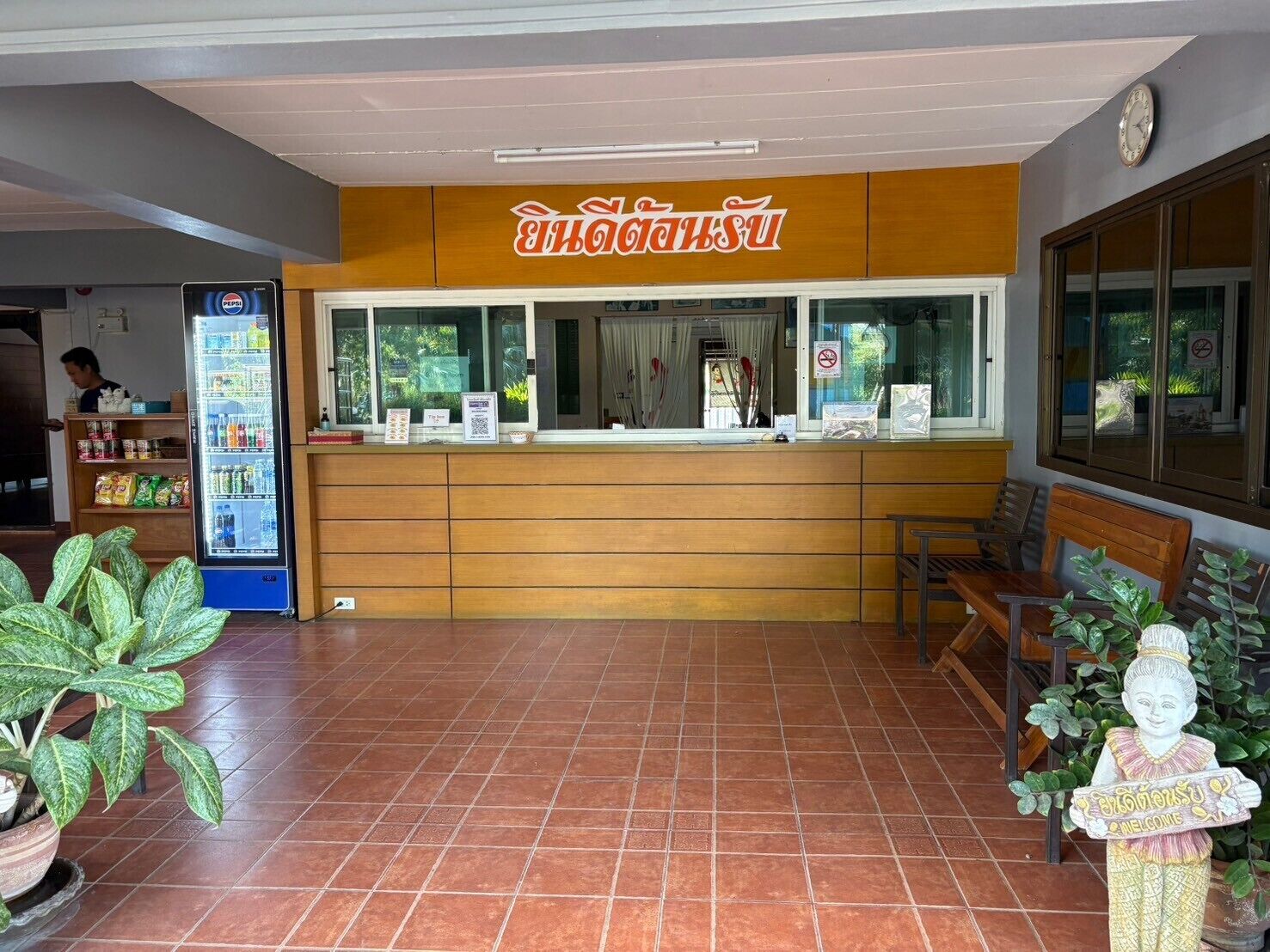 Zona de recepción con mostrador de madera, refrigerador de Pepsi y una estatua de un niño sosteniendo un cartel.