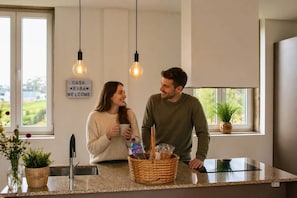 Une cuisine moderne avec un plan de travail en granit, des lampes suspendues, un panneau dâaccueil et une vue sur la verdure Ă lâextĂ©rieur.