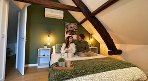 A bedroom with a sloped ceiling, a bed with a green and white patterned bedspread, bedside tables with lamps, and a poster on the wall.