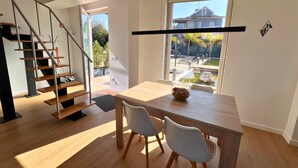 A modern interior with a staircase, a dining area with two chairs, a table with a bowl, and a large window with a view of the outside. - Casa da Eira - Rural Retreat (Vilar)