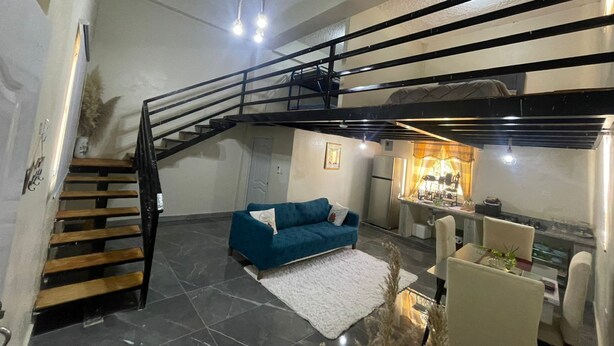 Amplia sala de estar con un sofá azul, una escalera, un comedor y una cocina.
