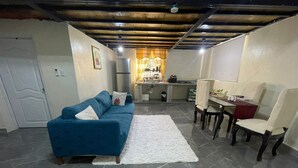 Un espacio habitable compacto con sofá azul, mesa de comedor con sillas, área de cocina y alfombra blanca.
