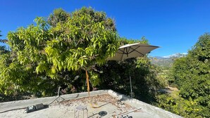 Una terraza en la azotea con piso de concreto, una silla de metal y un paraguas grande.