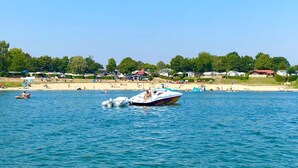 Un lac avec des bateaux, une plage de sable et des maisons en arrière-plan.