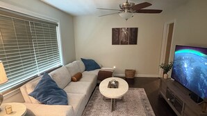 A living room with a sofa, coffee table, TV, ceiling fan, and artwork on the wall.