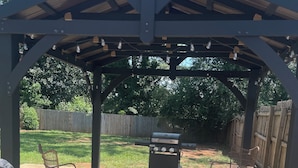 A covered patio area with a grill, two chairs, and a concrete floor.