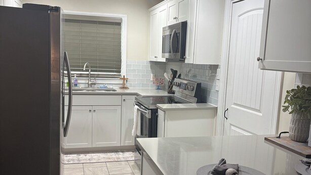 A modern kitchen with white cabinets, stainless steel appliances, and a tiled backsplash.