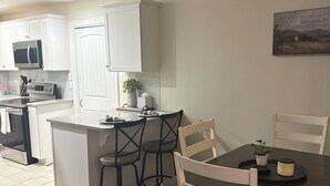 A modern kitchen with white cabinets, a microwave, and an oven. There is a dining area with a table and chairs.