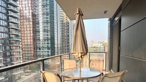 A balcony with a glass table and chairs, an umbrella, and a cityscape view. - *Cozy Condo/King Bed/Pool/Gym/CityViews/Walkscore 91 (Calgary)