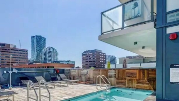 A rooftop pool with wooden deck, lounge chairs, and a city skyline view. - *Cozy Condo/King Bed/Pool/Gym/CityViews/Walkscore 91 (Calgary)