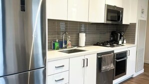 A modern kitchen with stainless steel appliances, white cabinets, a microwave, and a built-in oven. - *Cozy Condo/King Bed/Pool/Gym/CityViews/Walkscore 91 (Calgary)