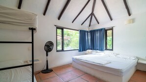 Een kamer met een stapelbed, een éénpersoonsbed, een ventilator en een raam met blauwe gordijnen.
