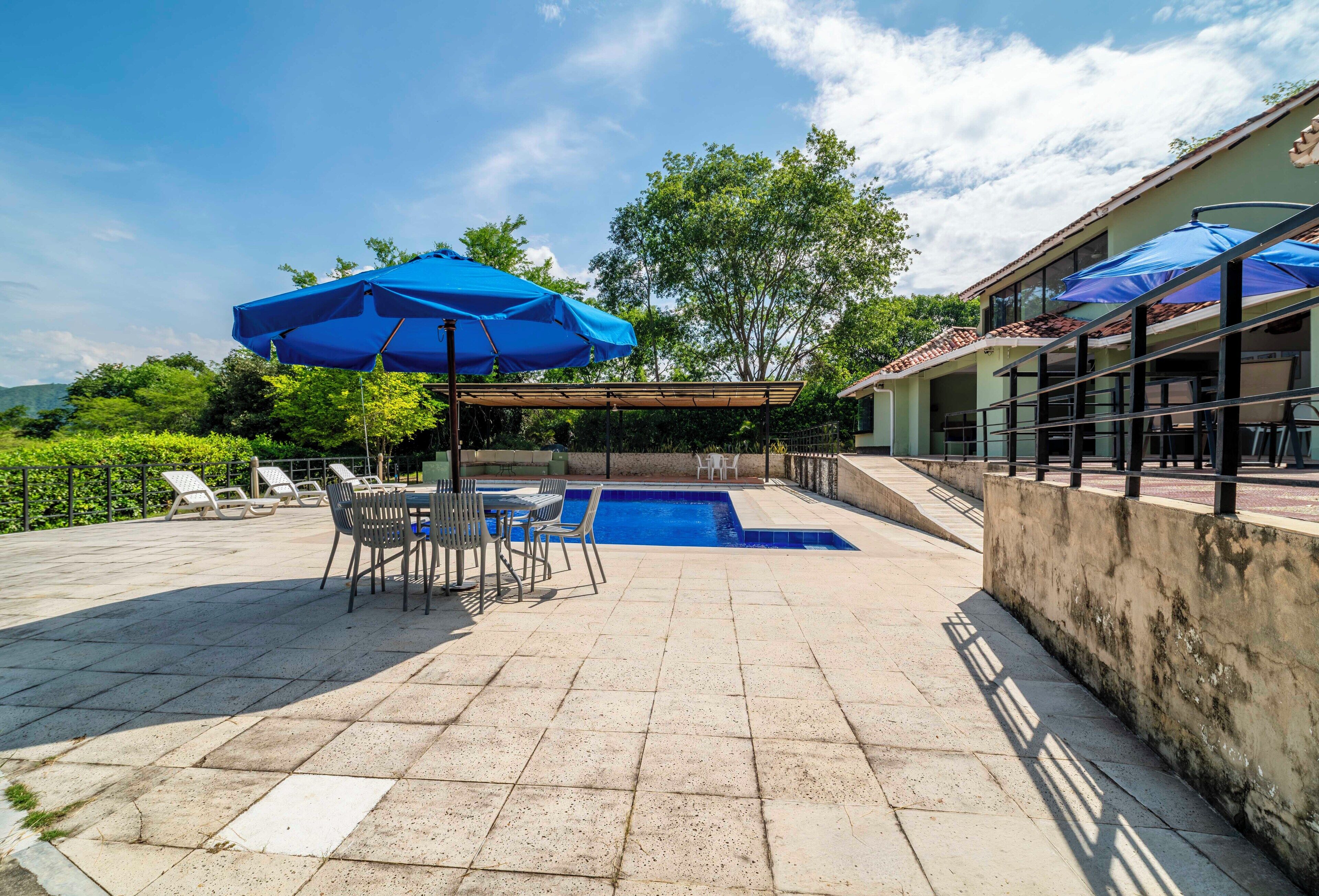 Ein Poolbereich mit blauen Sonnenschirmen, Liegestühlen und einer gefliesten Terrasse.