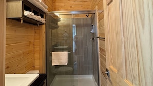 Een houten badkamer met een douchecabine van glas, een toilet en een plank met opgevouwen handdoeken.