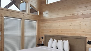 Een slaapkamer met een houten plafond, een groot bed met wit beddengoed, een nachtkastje en een raam.