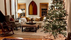 A cozy living room with a wooden floor, a large Christmas tree, a fireplace, and a ceiling fan. - Historic Edge of the River, Adirondacks (Willsboro)