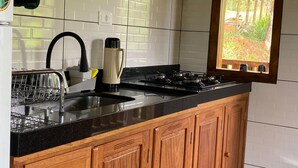 A kitchen with wooden cabinets, a black countertop, a sink, and a window with a view of greenery.