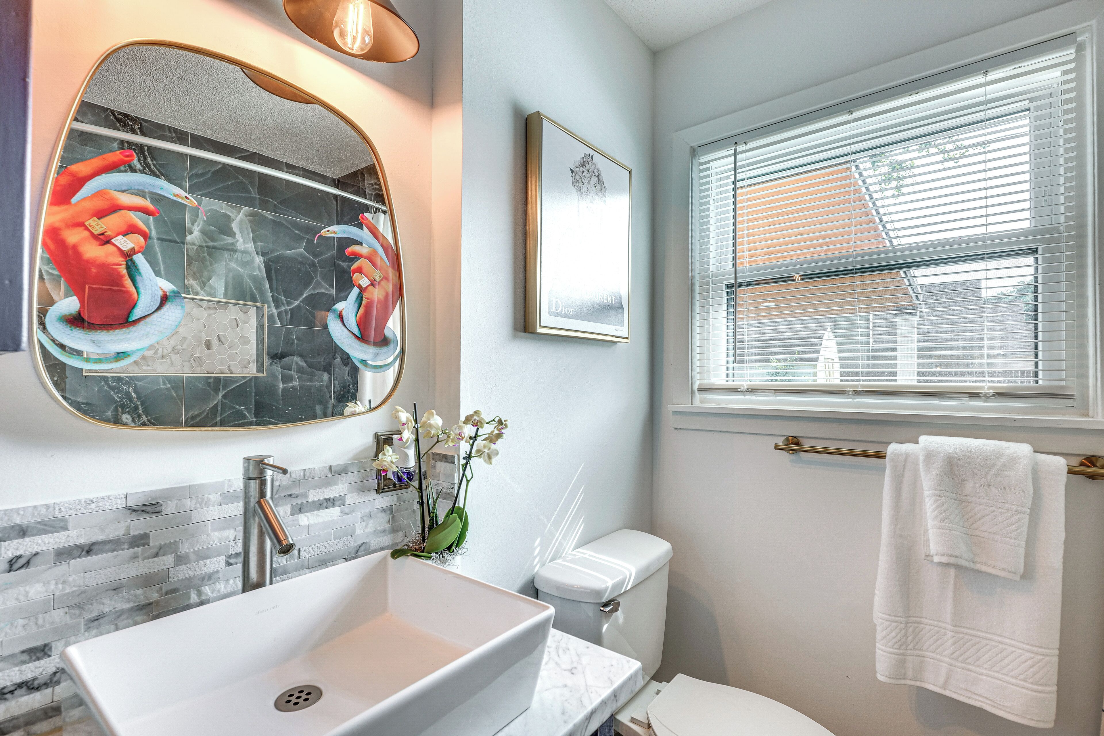 A bathroom with a large mirror, a sink, a toilet, and a window with blinds.
