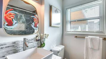 A bathroom with a large mirror, a sink, a toilet, and a window with blinds.
