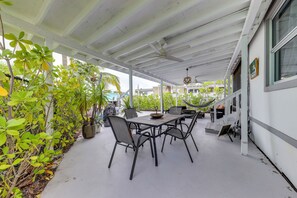En overdækket terrasse med spisebord og stole, omgivet af krukkeplanter og en hængekøje.