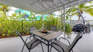 Une terrasse extérieure avec une table et des chaises, entourée de verdure et offrant une vue sur un bâtiment aux couleurs turquoises.