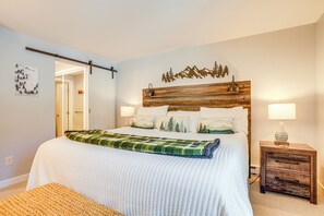 A bedroom with a bed, a wooden headboard, bedside lamps, a nightstand, and a door leading to another room. - Wintergreen Resort Condo: Deck & Golf Course Views (Wintergreen Resort)