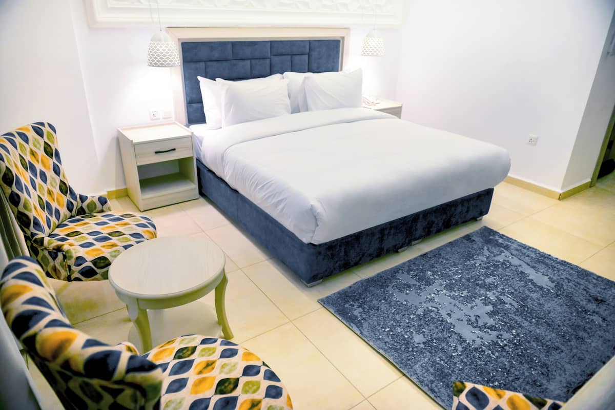 A bedroom with a bed, two chairs, a small table, and a rug.