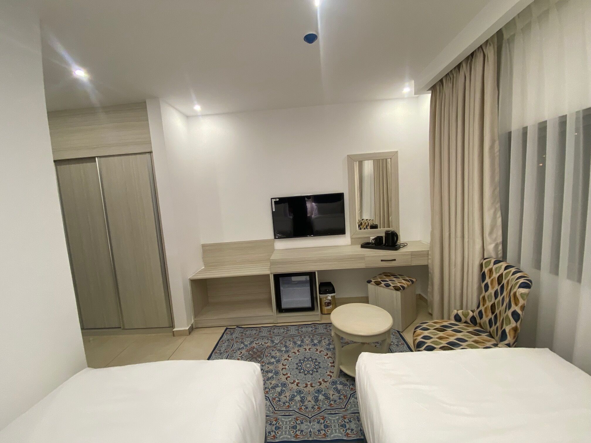 Une chambre d’hôtel avec deux lits, une télévision, un bureau avec un miroir, une petite table et un tapis à motifs.