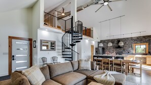A modern living room with a sectional sofa, a wooden coffee table, and a spiral staircase leading to an upper level. - Modern Cabin Near Cheney Lake W Pool and Hot Tub - Holiday Home (Pretty Prairie)