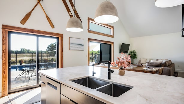 A modern kitchen with a large island, double sinks, and a dining area with a view of the outdoors. - Modern Cabin Near Cheney Lake W Pool and Hot Tub - Holiday Home (Pretty Prairie)