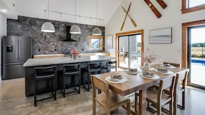 A modern kitchen with a stone backsplash, a central island, and a dining area with wooden furniture. - Modern Cabin Near Cheney Lake W Pool and Hot Tub - Holiday Home (Pretty Prairie)