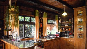 A rustic kitchen with wooden cabinets, a central island with a stove, and a window with curtains. - Charming 2-bedroom cabin in private condominium (Juayua)