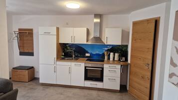 Eine kleine Küche mit weißen Schränken, einem eingebauten Ofen und einer Holztür.