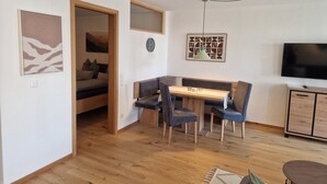 A compact living space with a dining area, a bed, a TV, and a door leading to another room.