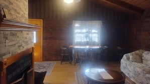 A cozy living room with a fireplace, wooden ceiling, and a dining area with a table and chairs. - Cold Spring Lodge - Cabin 5 (Big Indian)