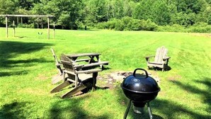 An outdoor area with a picnic table, two Adirondack chairs, and a portable grill.
