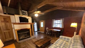 A cozy living room with a fireplace, wooden floors, a checkered sofa, and a dining area with a table and chairs.
