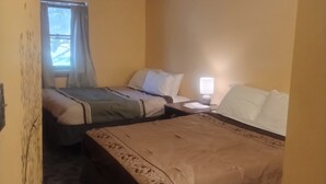 Camera d'albergo con due letti, una finestra con tende, un comodino con una lampada e un tappeto decorato.